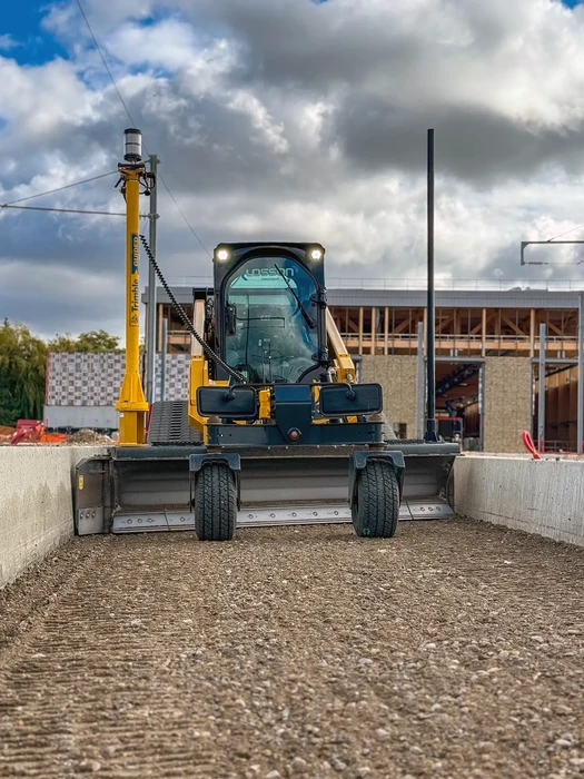 Chantier de construction extérieur avec engin de terrassement compact à chenilles équipé d'une foreuse hydraulique jaune positionnée sur dalle béton