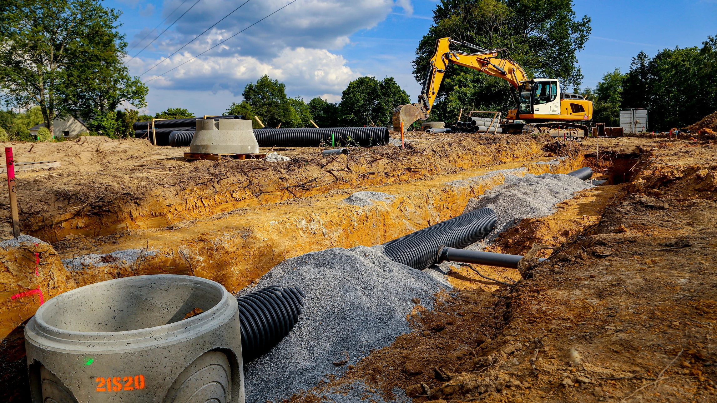 Chantier de construction extérieur avec pelleteuse orange sur roues pneumatiques creusant des tranchées dans terrain sablonneux